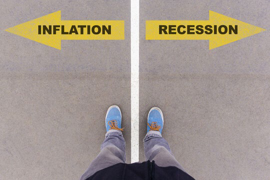 Photograph looking down at a person's feet standing on a line between two painted arrows labelled Inflation and Recession